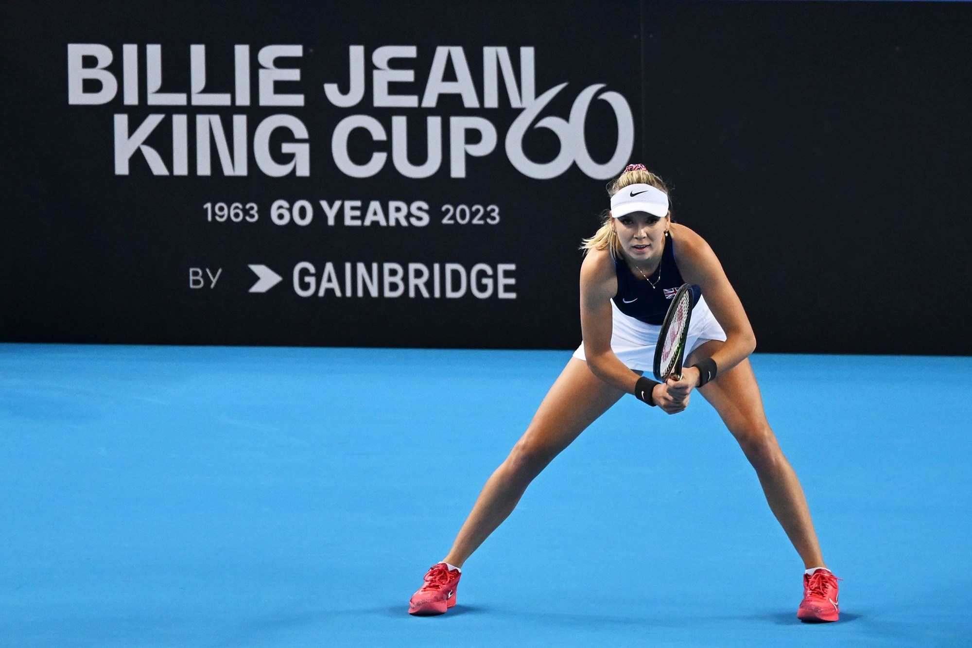Katie Boulter stood in front of a Billie Jean King Cup advertisement board while preparing to return a serve on court