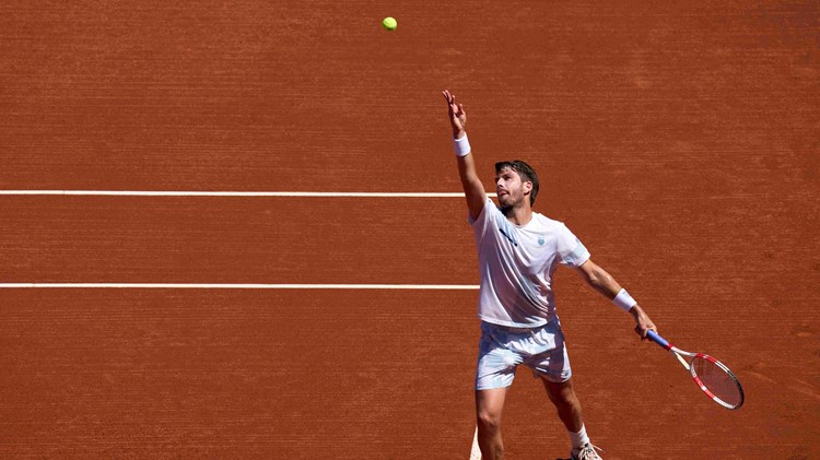 Cam Norrie serving on a clay court while holding his racket