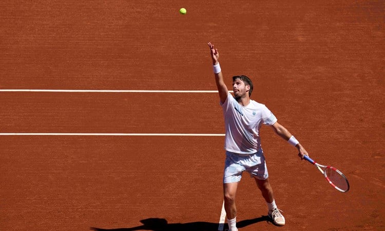 Cam Norrie serving on a clay court while holding his racket