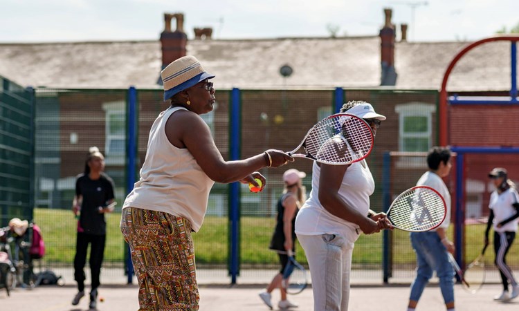 An image of a group of ladies holding tennis rackets and balls on a concrete tennis court group session