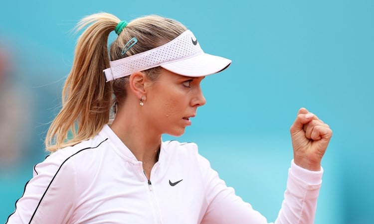 Katie Boulter, wearing a white Nike fleece and hat, clenching her fist in celebration on court at the Madrid Open