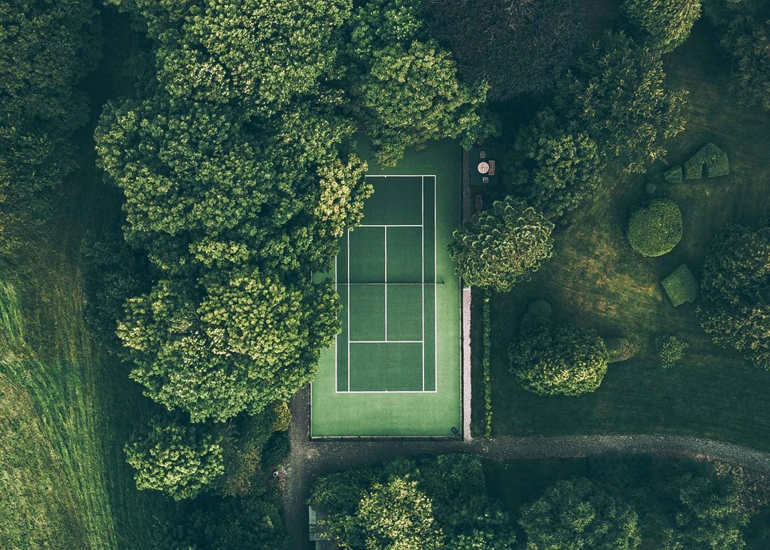 A green tennis court surrounded by green trees and grass