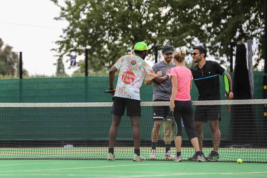 Four people shaking hands on a tennis court at the net