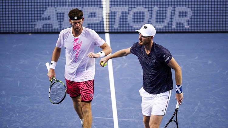 Jamie Murray and Michael Venus stood fist bumping on court with an ATP Tour branded tennis net behind them