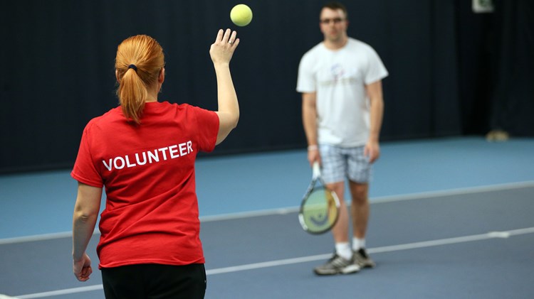Volunteer helping visually impaired tennis players