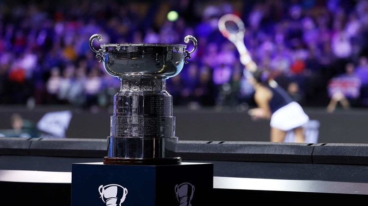 The Billie Jean King Cup 2022 trophy on its stand in front of a tennis player serving