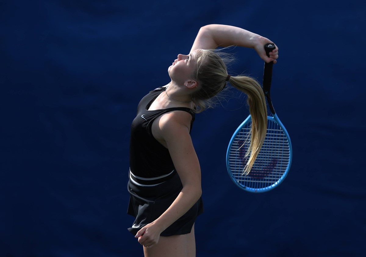 Junior player jumps and reaches for a shot with racket behind her back