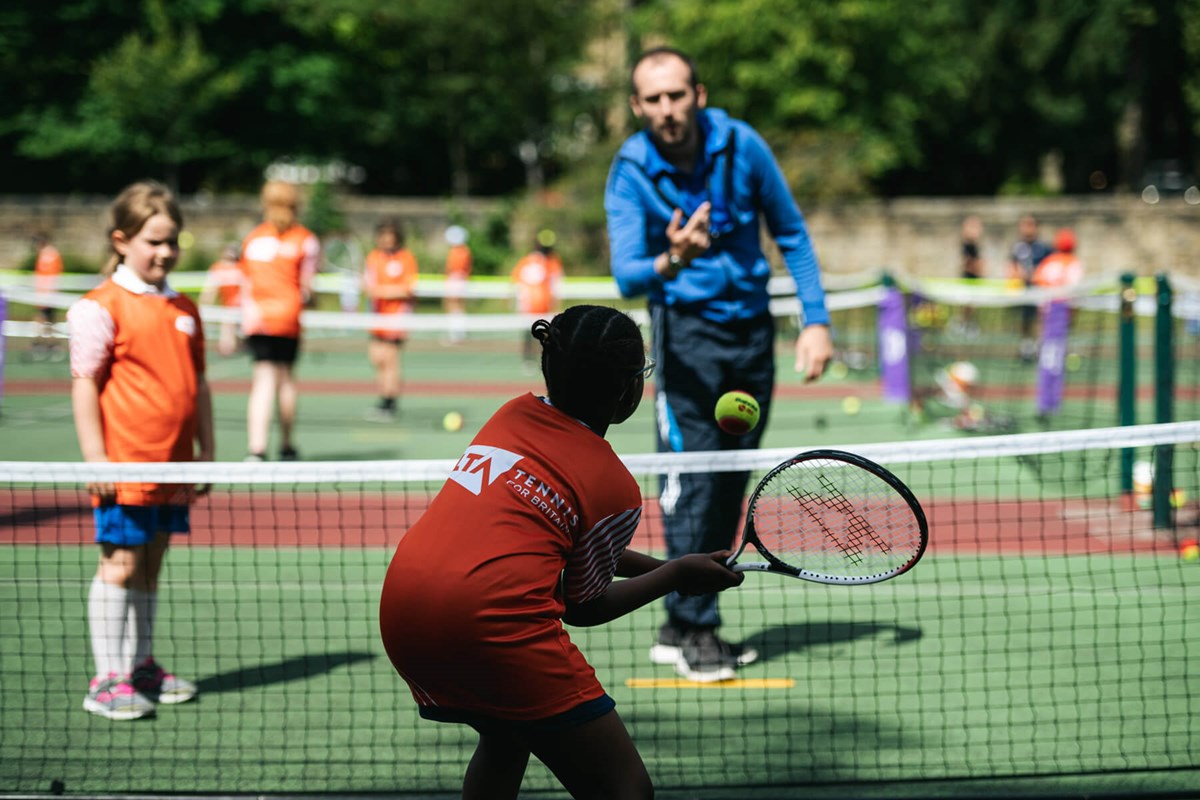 Coach throws ball to girl over net