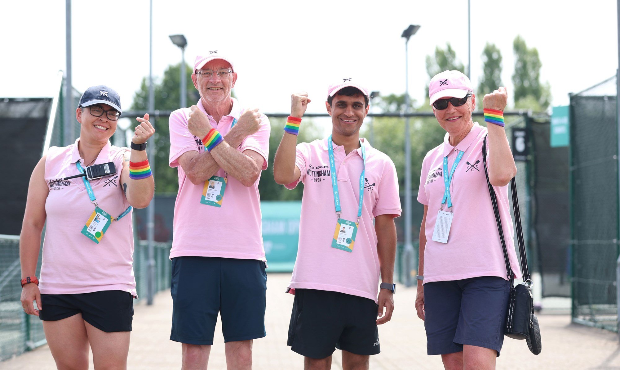 A group of four volunteers smiling and showing off their Pride rainbow wristbands