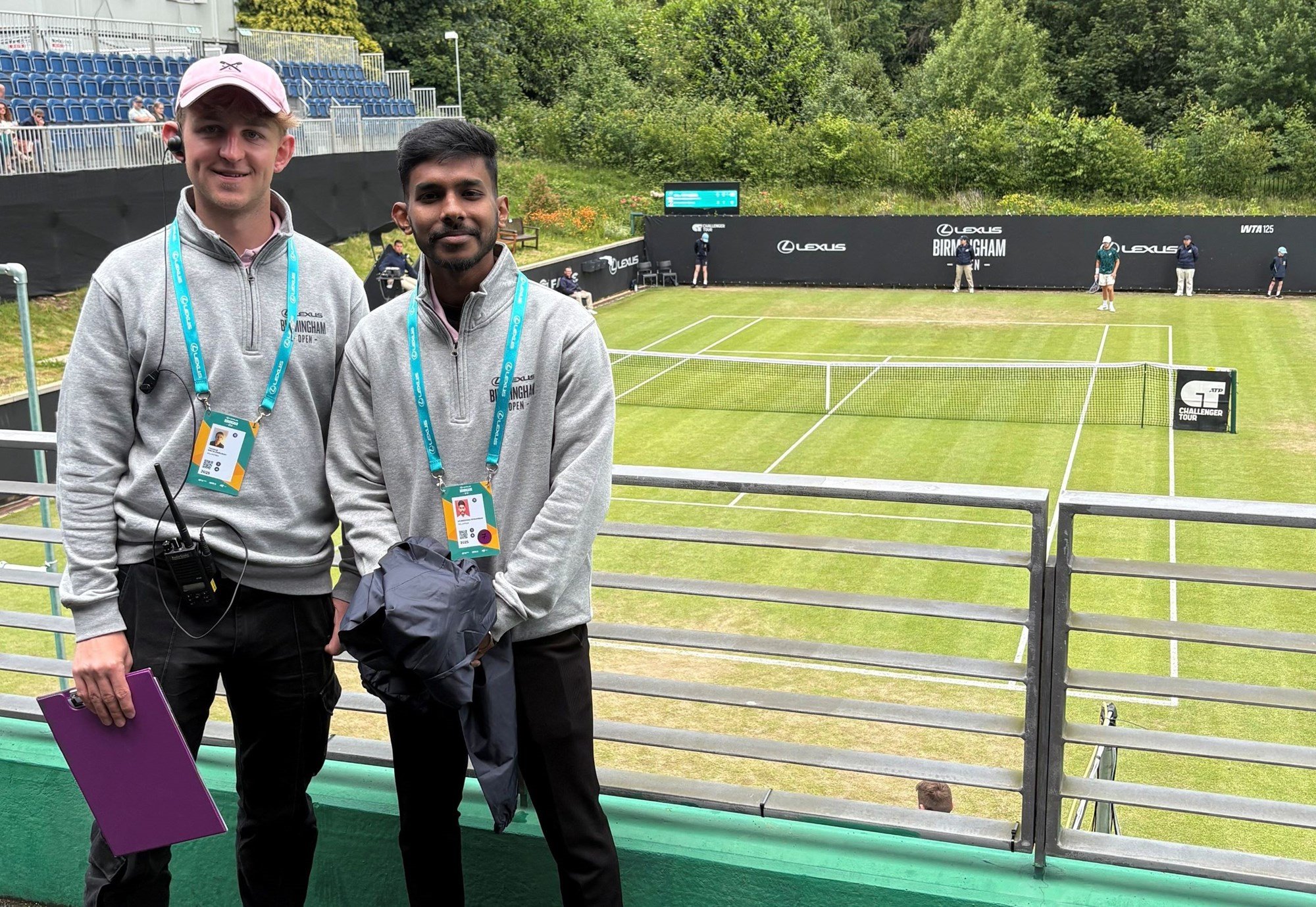 Two young male volunteers standing in the stands with the court behind them at the Lexus Birmingham Open