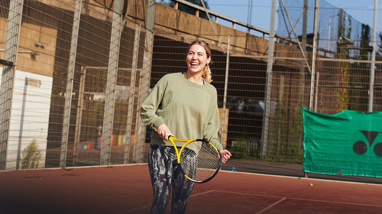 Woman laughing on tennis court holding racket