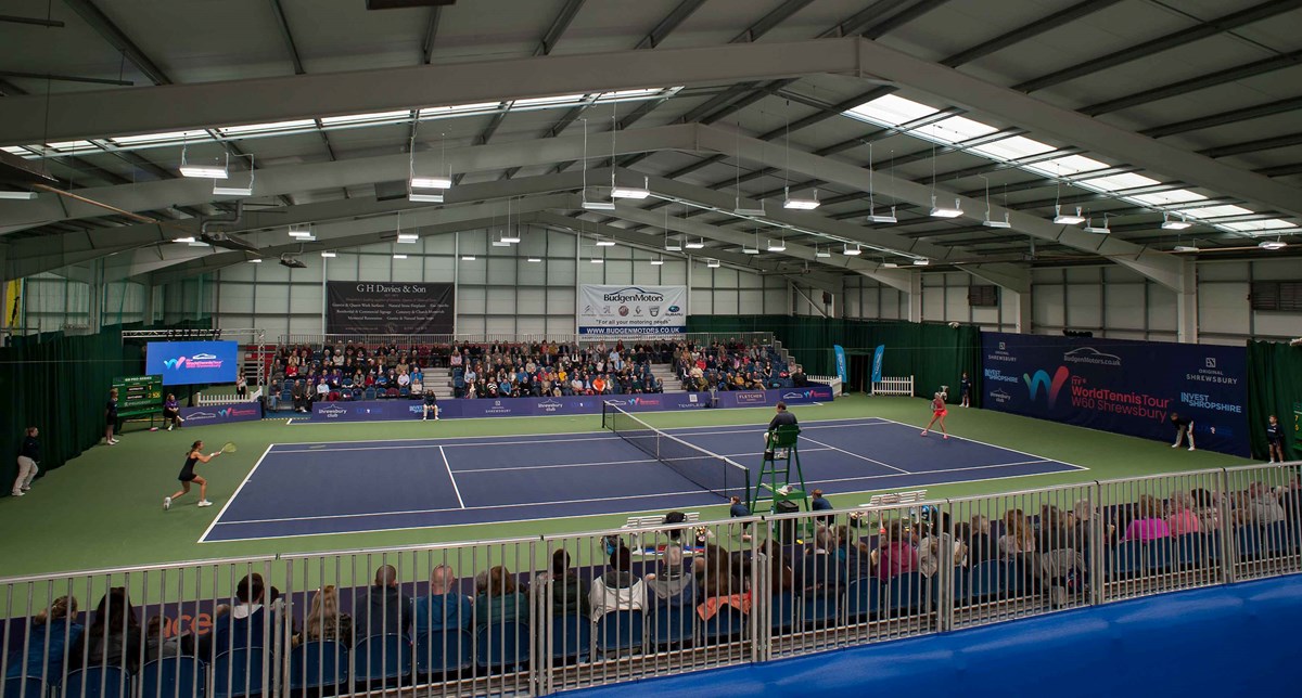 Two female tennis players playing a match on an indoor tennis court in front of a crowd