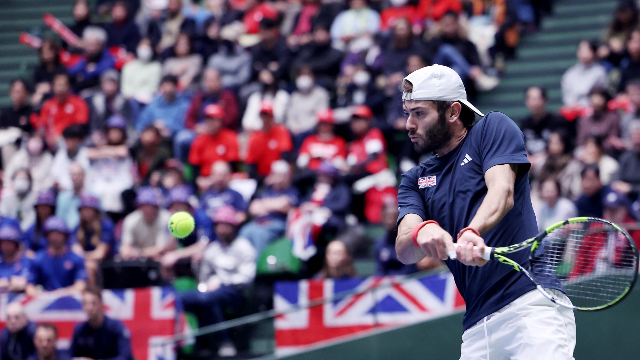 Jacob Fearnley preparing to hit a backhand at the Davis Cup with multiple Great Britain flags in the background