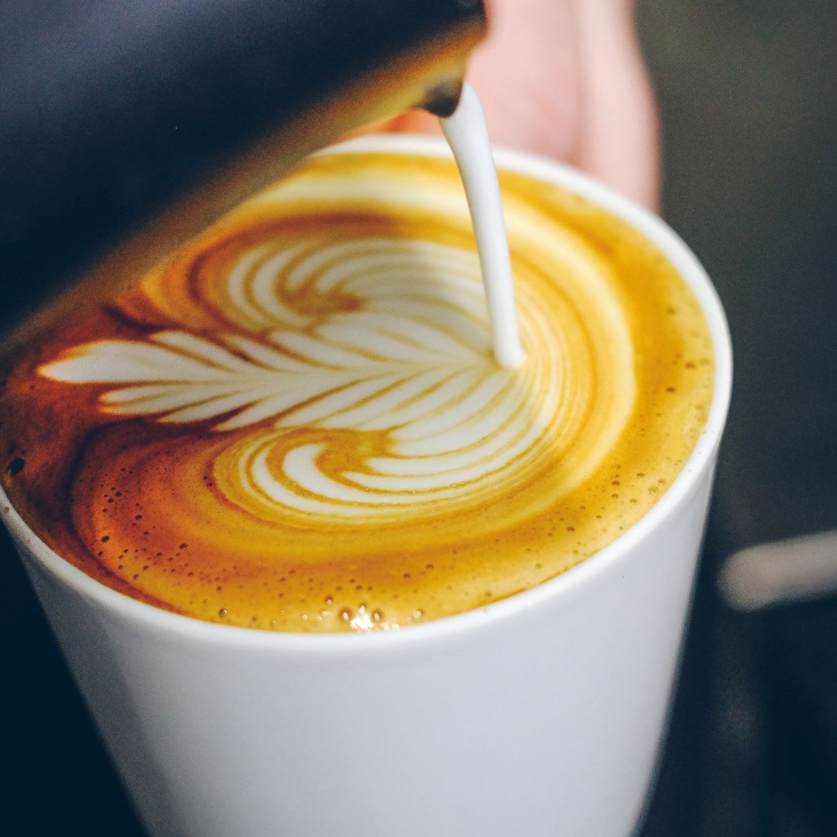 Hot milk being poured into a coffee with some latte art on top
