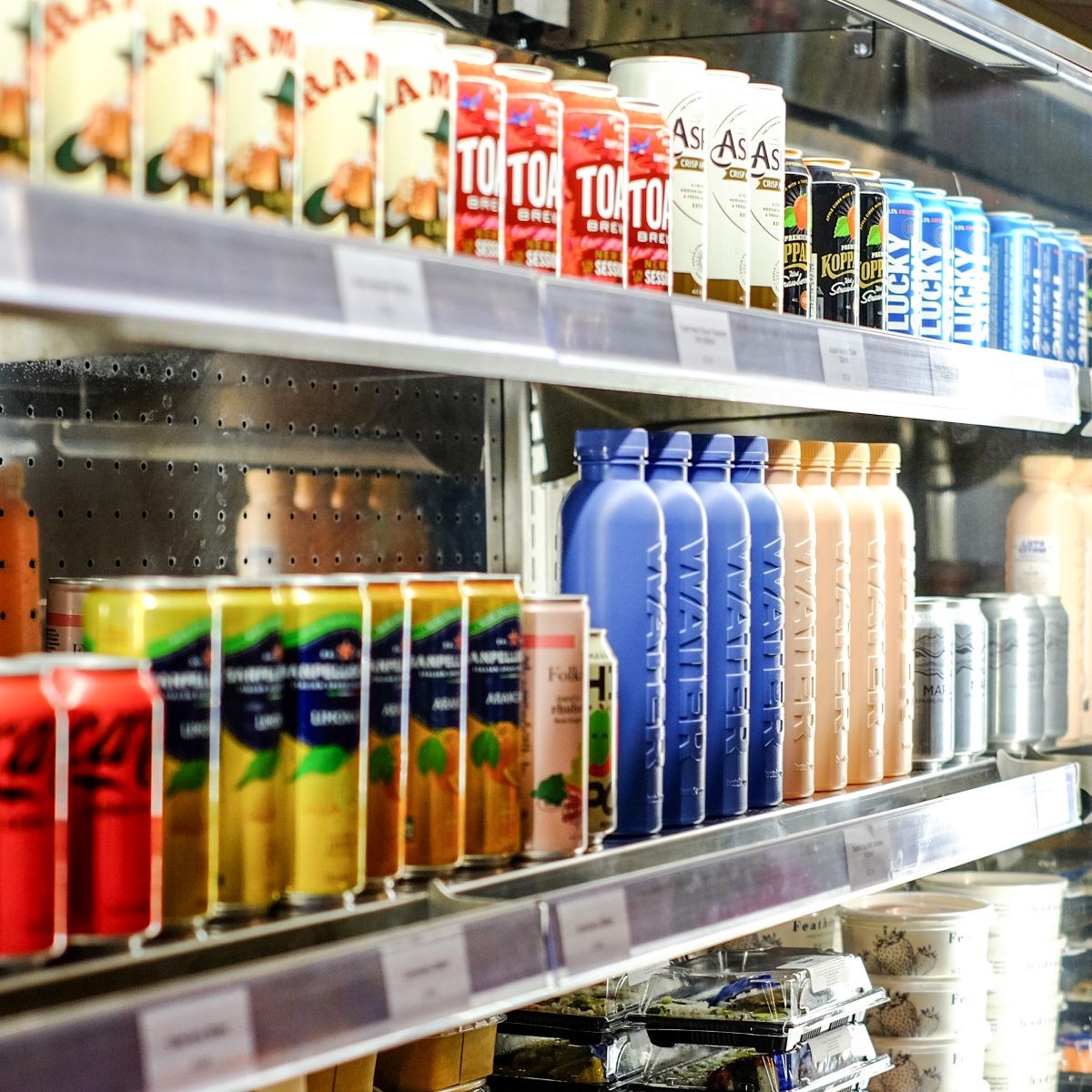 An open fridge filled with cold drink cans and bottles