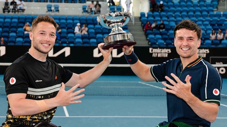 Alfie Hewett and Gordon Reid holding their Australian Open trophy while showing five fingers on their hands to signify five successive Aus Open titles