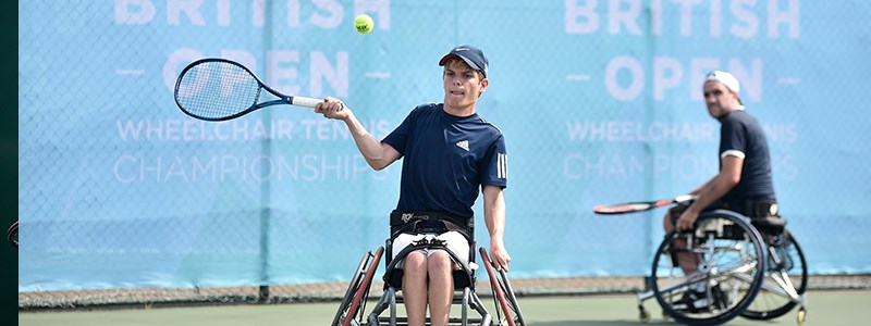 Greg Slade about to play a forehand shot with Gordon Reid watching in the background