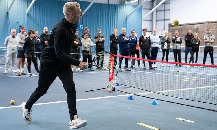 Male coach on mini tennis court demonstrating drill to crowd