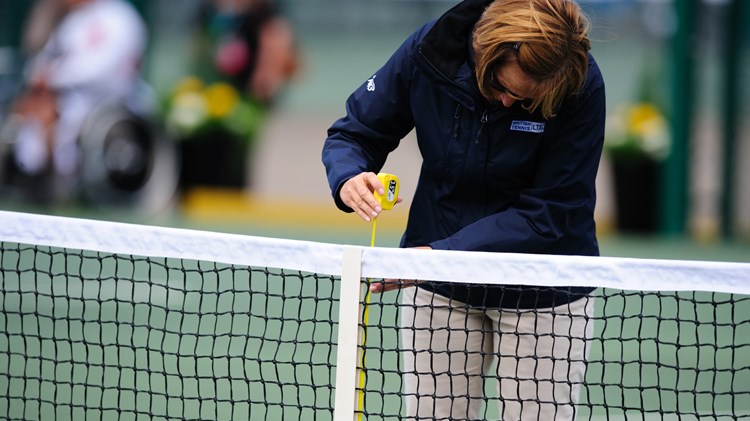 A tennis official measuring the height of a tennis net