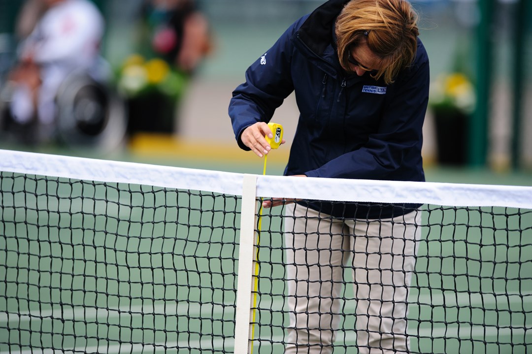 A tennis official measuring the height of a tennis net