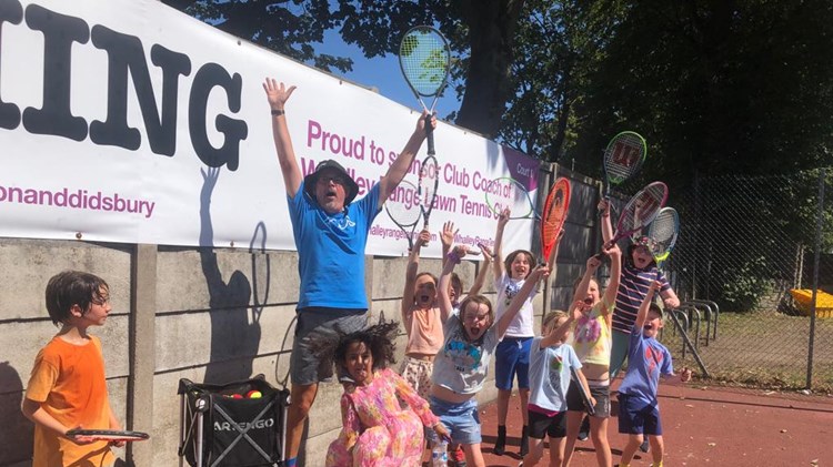 Head Coach of Whalley Tennis Club, Simon Wood, celebrating with the kids from his youth sessions while they wave their rackets in the air. 