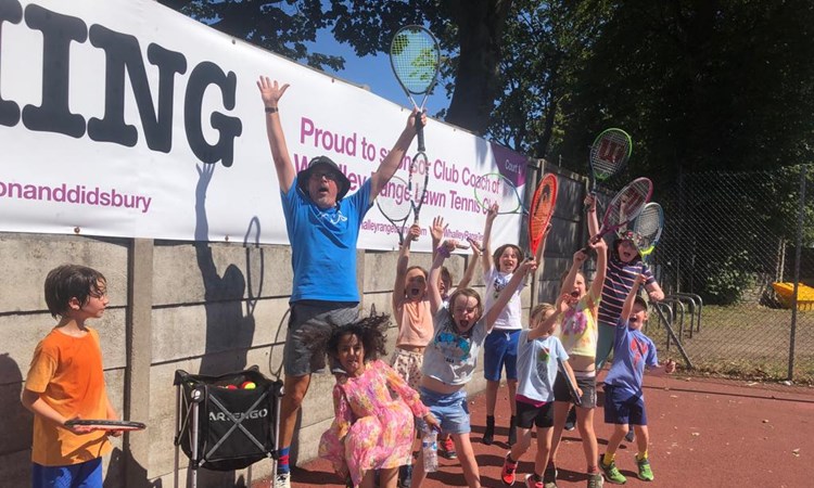 Head Coach of Whalley Tennis Club, Simon Wood, celebrating with the kids from his youth sessions while they wave their rackets in the air. 