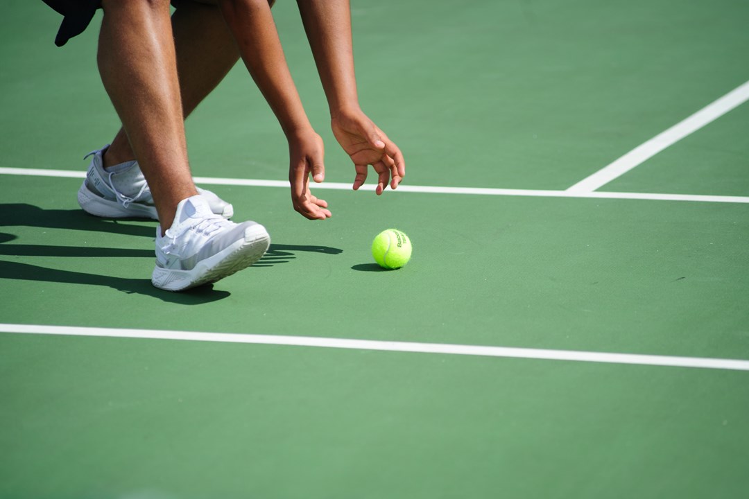 A ball girl picking up a tennis ball on a hard court