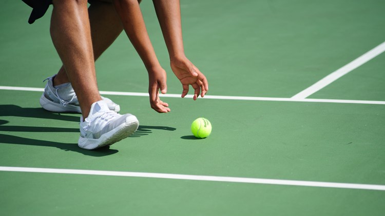 A ball girl picking up a tennis ball on a hard court