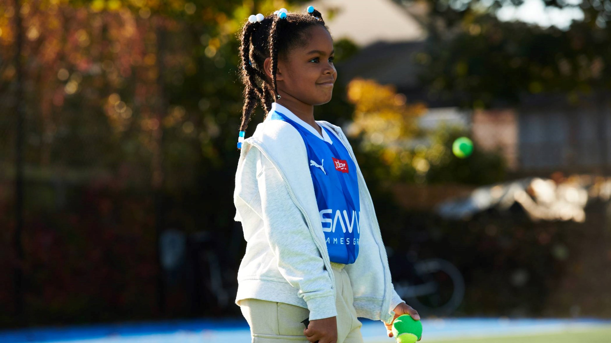 Young girl smiling on court with a tennis racket and ball