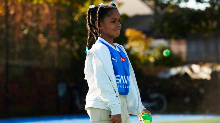 Young girl smiling on court with a tennis racket and ball