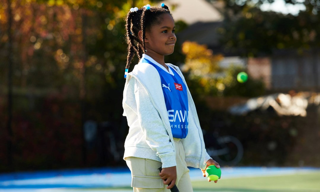 Young girl smiling on court with a tennis racket and ball