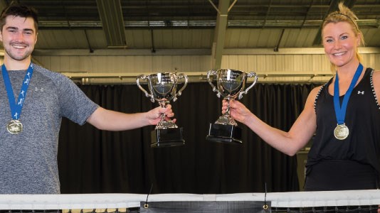 A male and a female tennis player wearing medals and holding up their trophies from the Tennis Scotland Open Tour. 