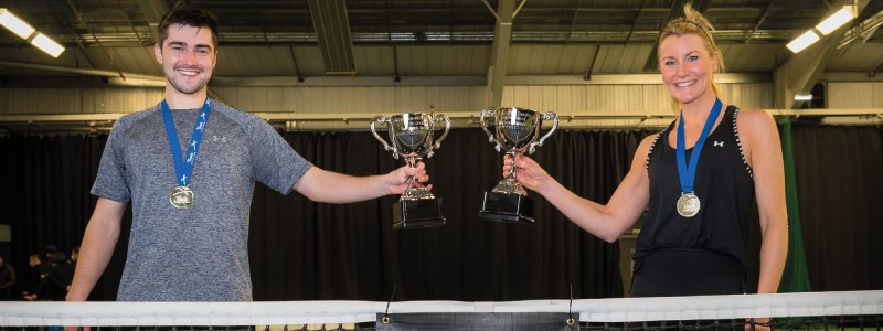 A male and a female tennis player wearing medals and holding up their trophies from the Tennis Scotland Open Tour. 