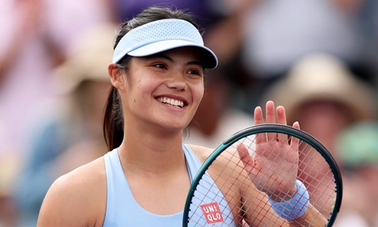 Emma Raducanu smiling while clapping her tennis racket on court at the BNP Paribas Open Indian Wells