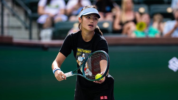 Emma Raducanu preparing to hit a serve while wearing a hat on court at the BNP Paribas Open Indian Wells