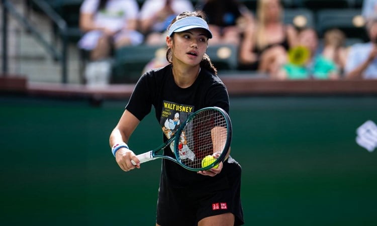Emma Raducanu preparing to hit a serve while wearing a hat on court at the BNP Paribas Open Indian Wells