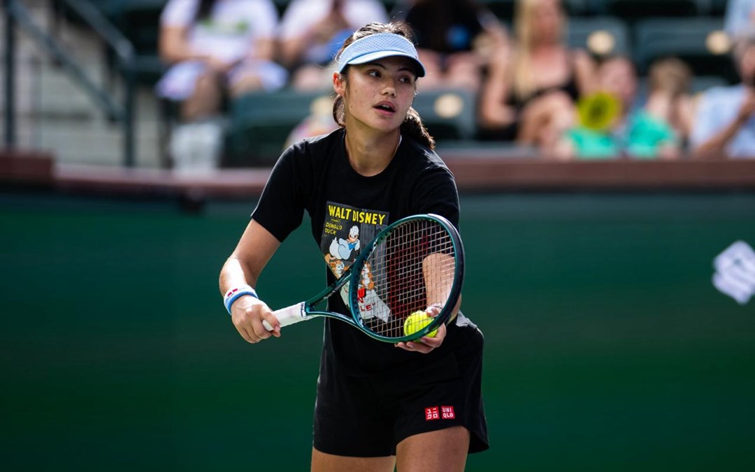 Emma Raducanu preparing to hit a serve while wearing a hat on court at the BNP Paribas Open Indian Wells