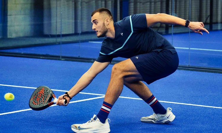 Louie Harris bending down to retrieve a ball with his padel bat on court