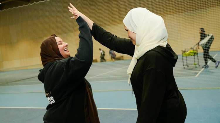Two women smiling and high five each other on tennis court
