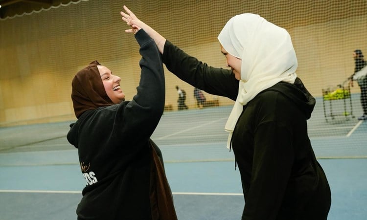 Two women smiling and high five each other on tennis court