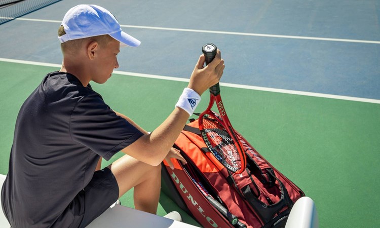 A junior tennis player taking a tennis racket out of a bag