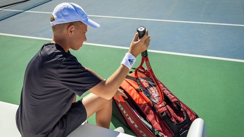A junior tennis player taking a tennis racket out of a bag