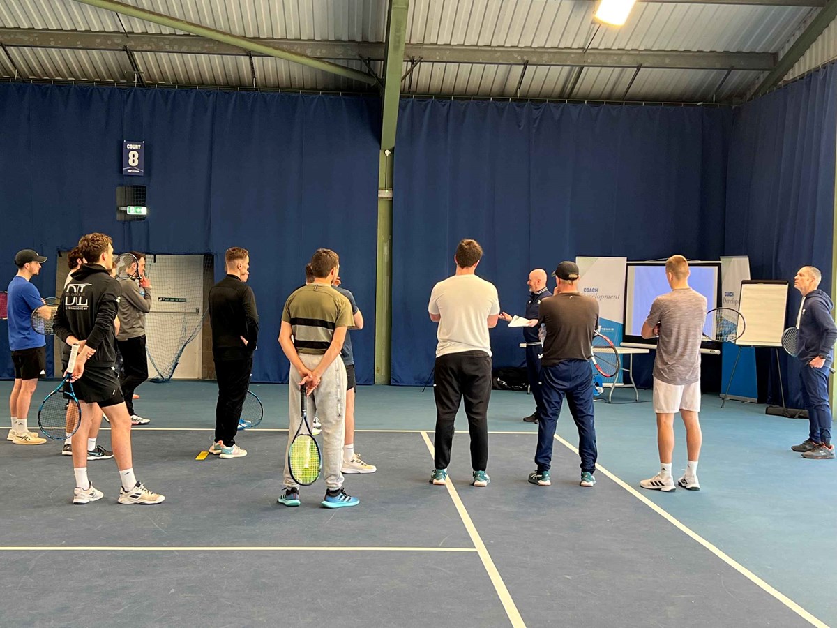 Tennis coaches standing on court learning about performance coaching at a training session