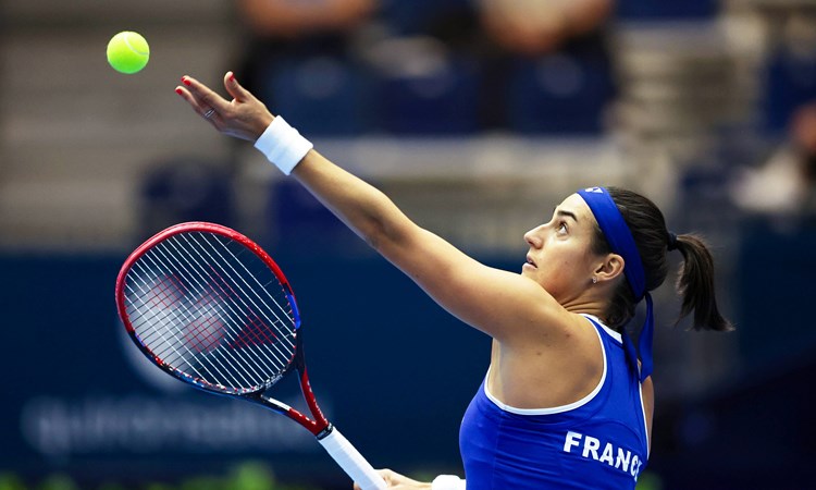 Caroline Garcia wearing a blue top with 'France' written on the back preparing to serve on court at the Billie Jean King Cup Finals 