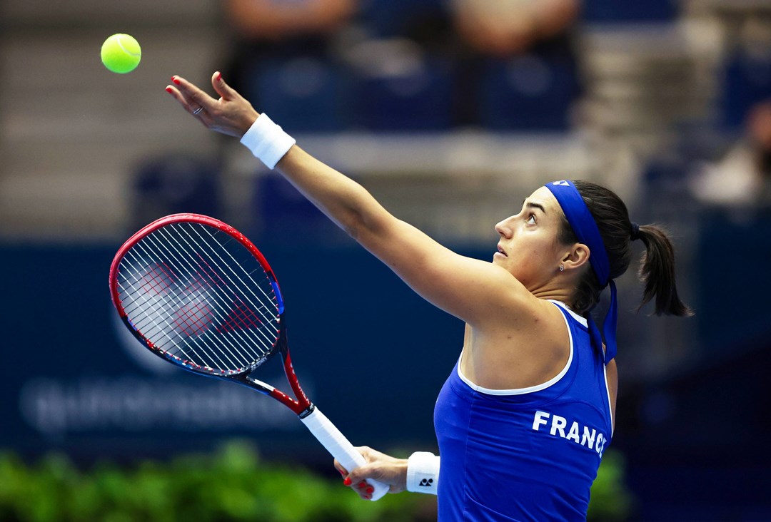 Caroline Garcia wearing a blue top with 'France' written on the back preparing to serve on court at the Billie Jean King Cup Finals 