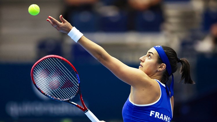Caroline Garcia wearing a blue top with 'France' written on the back preparing to serve on court at the Billie Jean King Cup Finals 