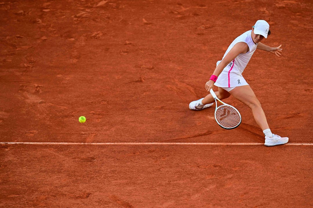 Iga Swiatek sliding to hit a backhand slice on a clay court at Roland Garros