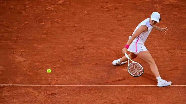 Iga Swiatek sliding to hit a backhand slice on a clay court at Roland Garros
