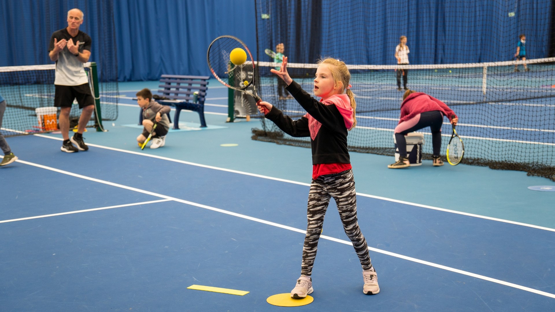 a young girl watches a sponge ball onto her racket