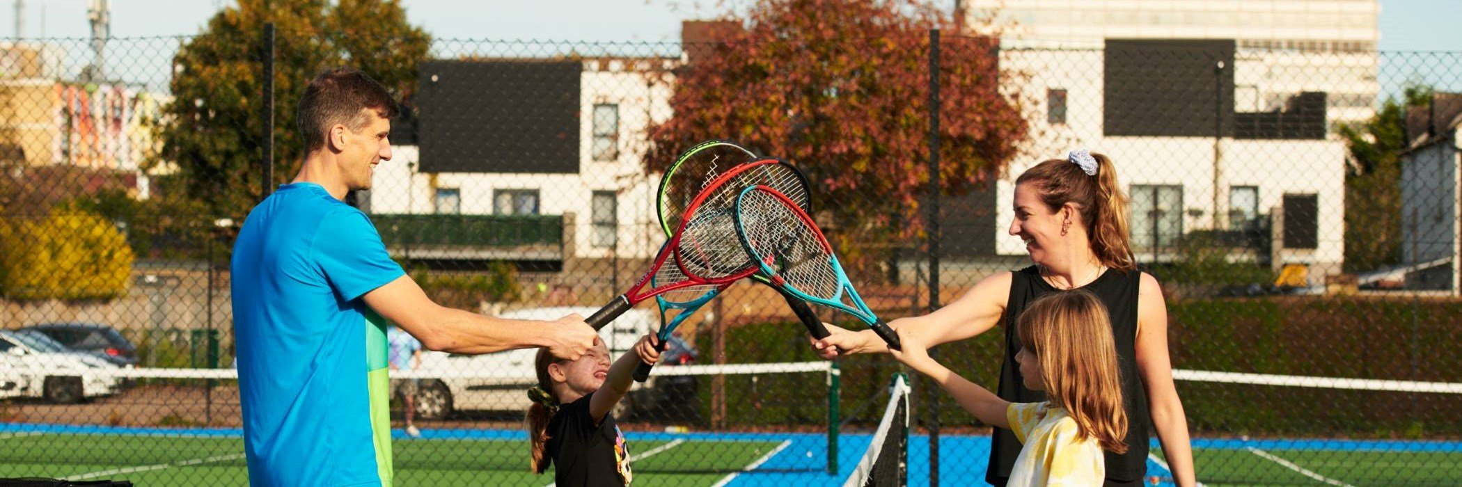 A family touching rackets at the net after playing a game of tennis